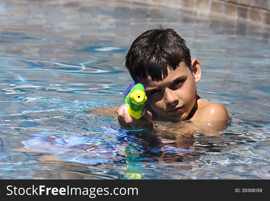 A 9 year old boy playing in the pool with a water gun. A 9 year old boy playing in the pool with a water gun.