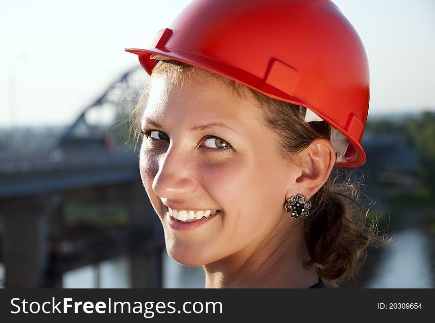 Young architect-woman wearing a protective helmet standing on the bridge background is smiling