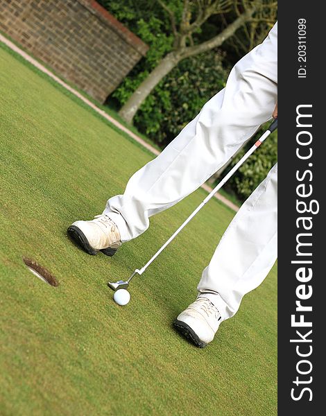 Image of a golfer standing on the green in bright sunlight putting the ball