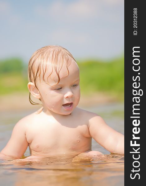 Adorable baby sit in river and play with sand and wood branch