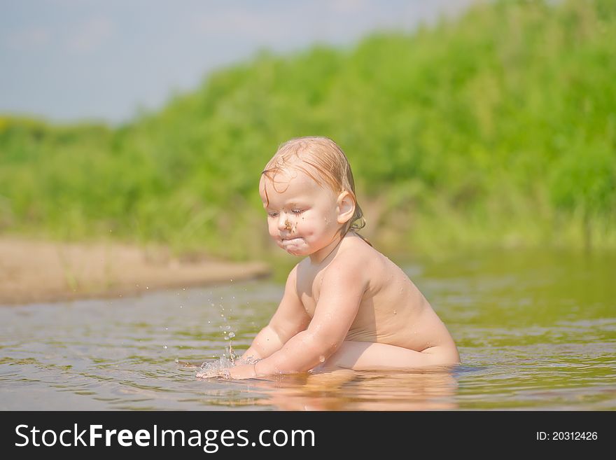 Adorable baby sit in river and play with sand and water