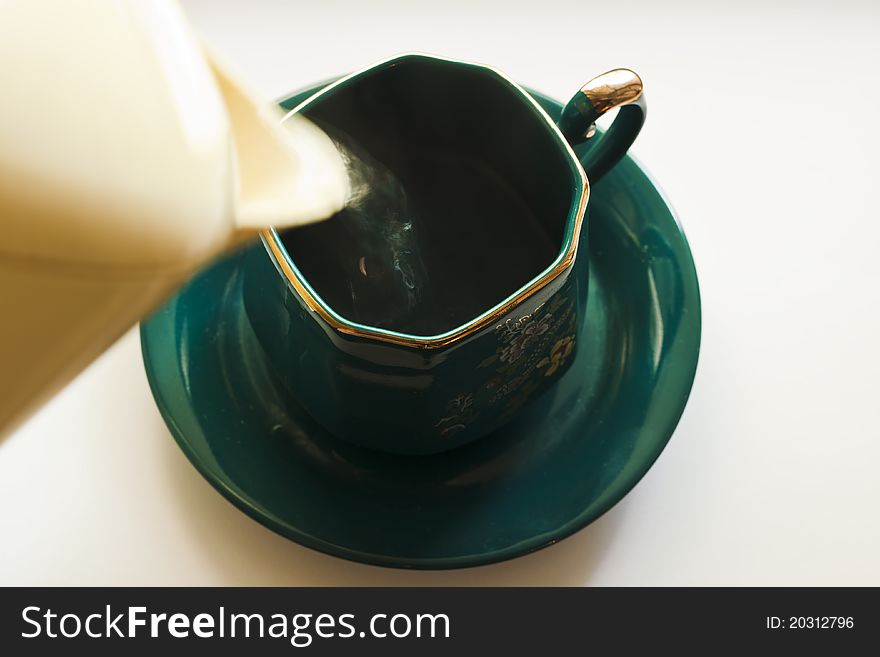 Boiling water is poured from a teapot into a green cup on a saucer