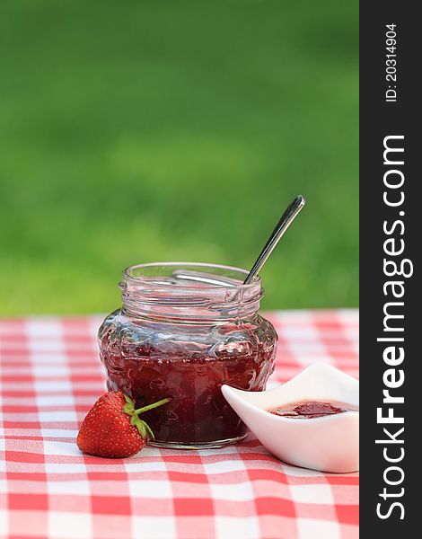 Jar of strawberry jam on the table in the summer garden