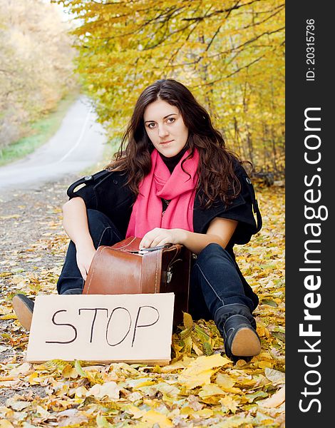 Woman hitchhiking sitting in an autumn bright leaves. Woman hitchhiking sitting in an autumn bright leaves