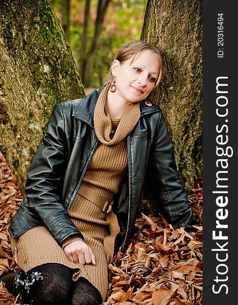 Young woman sitting in autumn leaves and leaning against a tree. Young woman sitting in autumn leaves and leaning against a tree