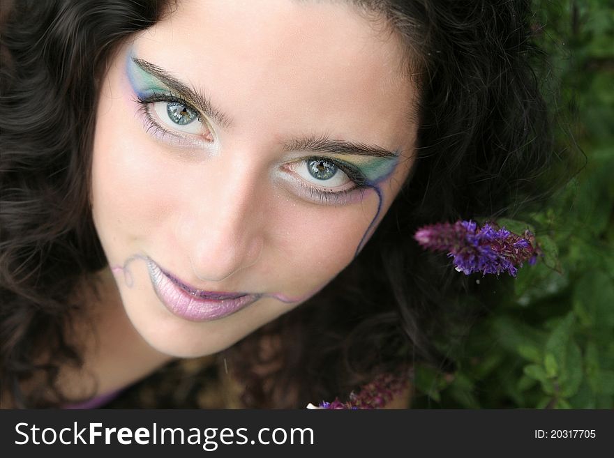 A young woman looking up secretively, a purple flower close to her, a pale rainbow of color on her face.