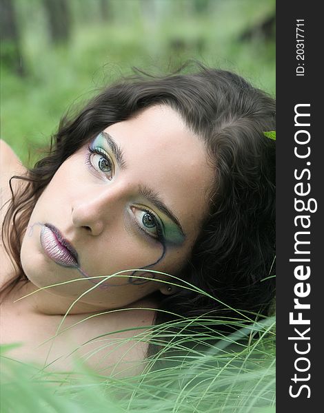 Young woman laying in the grass after the rain, a pale rainbow of makeup on her face.