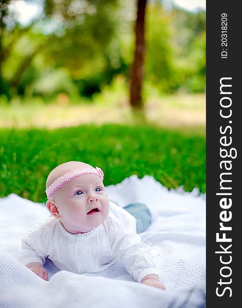 Little baby girl with pink headband lying on her belly on a white counterpane and looking up. Little baby girl with pink headband lying on her belly on a white counterpane and looking up