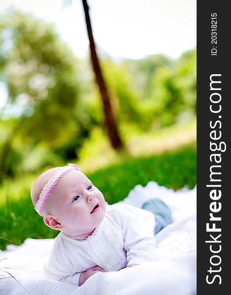 Little baby girl with pink headband lying on her belly on a white counterpane and looking up