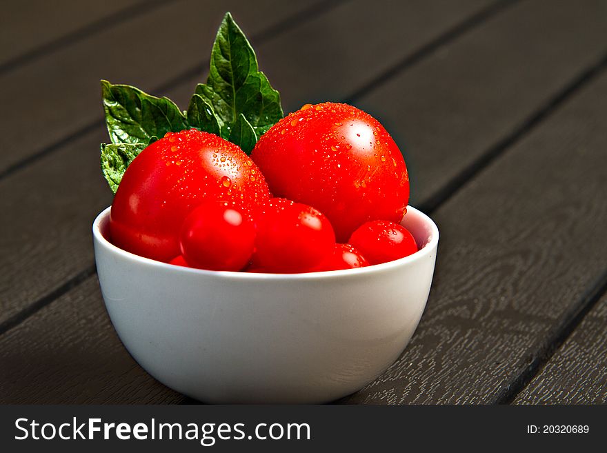 White bowl with fresh tomatoes and leaves on black table. White bowl with fresh tomatoes and leaves on black table