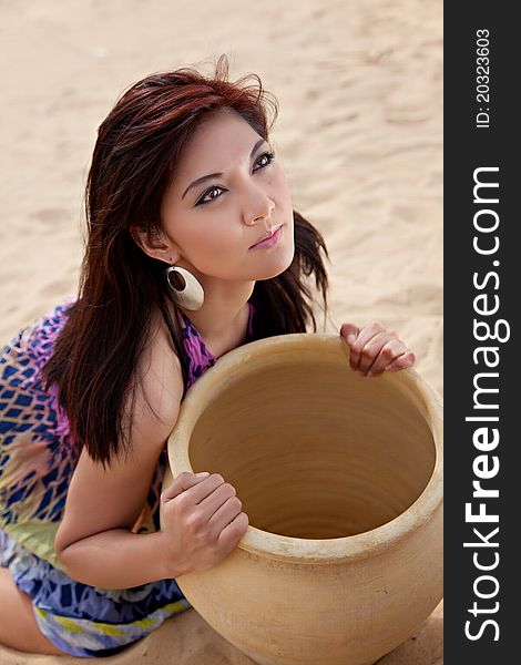 Asian female holding a large water clay pot outside on the sand. Asian female holding a large water clay pot outside on the sand