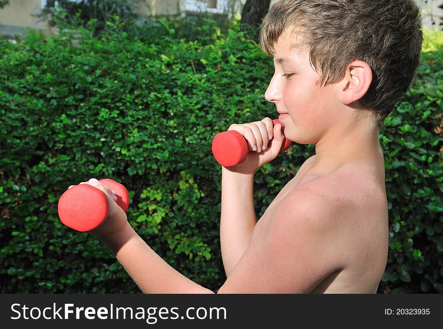 A boy plays sports in the yard of red dumbbell raises. A boy plays sports in the yard of red dumbbell raises