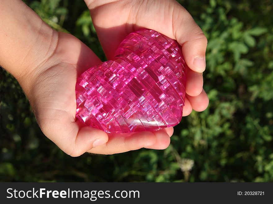 Children\'s hands carefully holding a toy heart. Children\'s hands carefully holding a toy heart