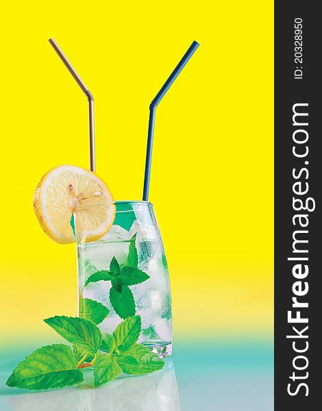 Fresh drink with mint, lemon and ice on yellow background