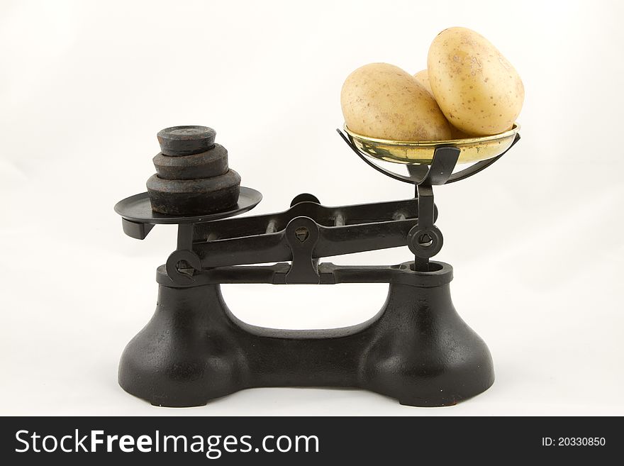 An old weighing scales painted black with a brass bowl containing potato tubers all isolated on white. An old weighing scales painted black with a brass bowl containing potato tubers all isolated on white.