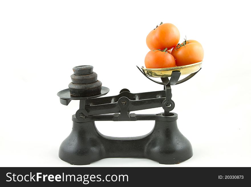 An old weighing scales painted black with a brass bowl containing tomatoes all isolated on white. An old weighing scales painted black with a brass bowl containing tomatoes all isolated on white.