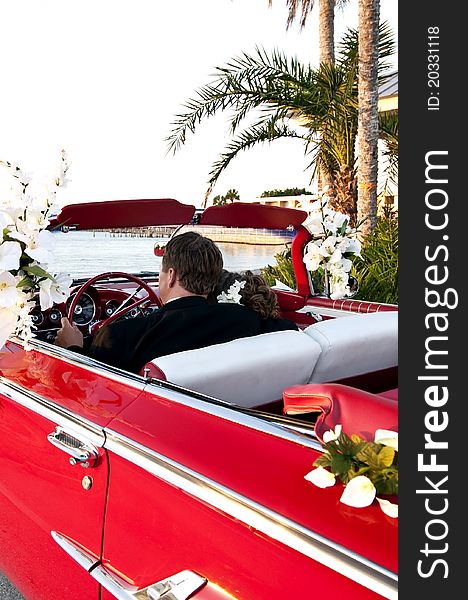 Bride and groom sitting in a red convertible overlooking the ocean. Bride and groom sitting in a red convertible overlooking the ocean.