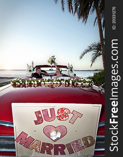 Bride and groom sitting in a red convertible celebrating and overlooking the ocean. Bride and groom sitting in a red convertible celebrating and overlooking the ocean.