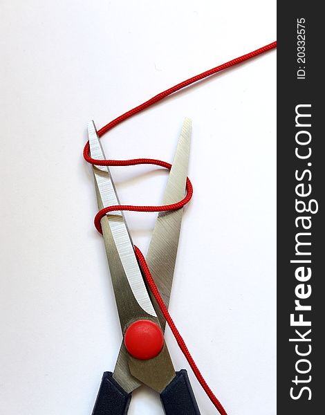 A scissors cutting red thread. A scissors cutting red thread