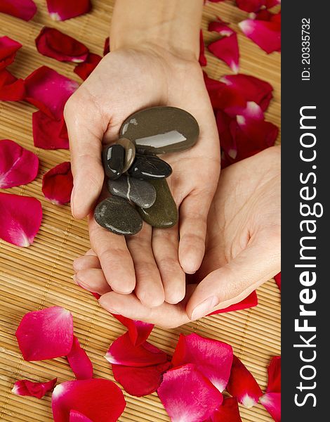 Close-up of beautiful girls hands are on red rose petals. In the hands of the stones are. Close-up of beautiful girls hands are on red rose petals. In the hands of the stones are