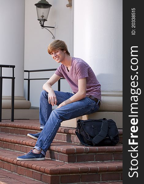 Vertical photograph of a male college student sitting on steps outside in front of a school building. Vertical photograph of a male college student sitting on steps outside in front of a school building