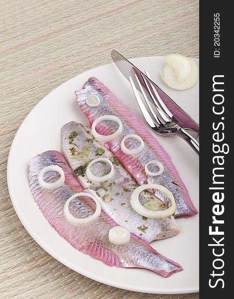 Studio-shot of a plate with matjes herring fillets with onions. Matjes in beetroot juice and matjes in herbal sauce.