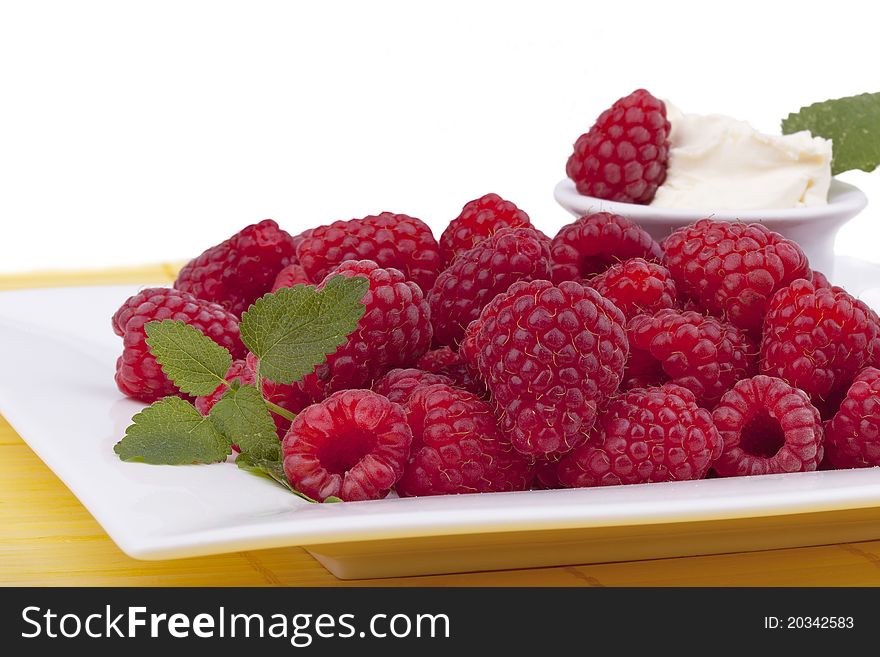 Studio-shot of a plate with raspberries garnished with lemon balm and a small bowl of sweet mascarpone, isolated on white.