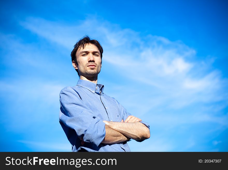 Young business man in a blue shirt against the blue sky. a symbol of leadership, success and freedom.