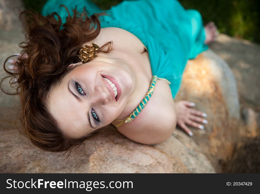 Beautiful brunette girl in a blue dress lying on a rock