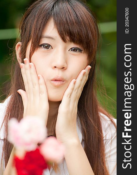 Young healthy Thai girl portrait in the park with flowers, focus at Model, hands on her cheek. Young healthy Thai girl portrait in the park with flowers, focus at Model, hands on her cheek