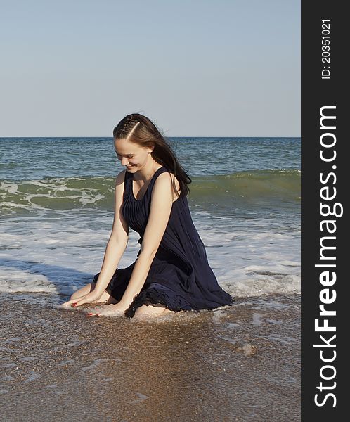 Beautiful young girl in black wet dress sits in water of the sea