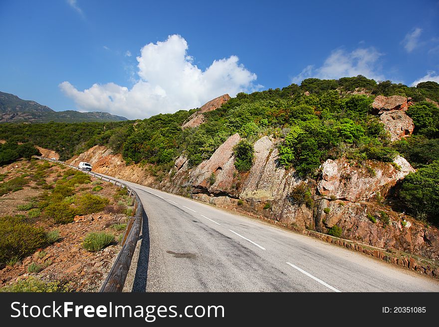 Rock cliff paved road with greenery in Corsica with blue skies. Rock cliff paved road with greenery in Corsica with blue skies.