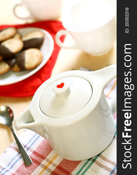 Teapot with red heart, cup and cookies on table