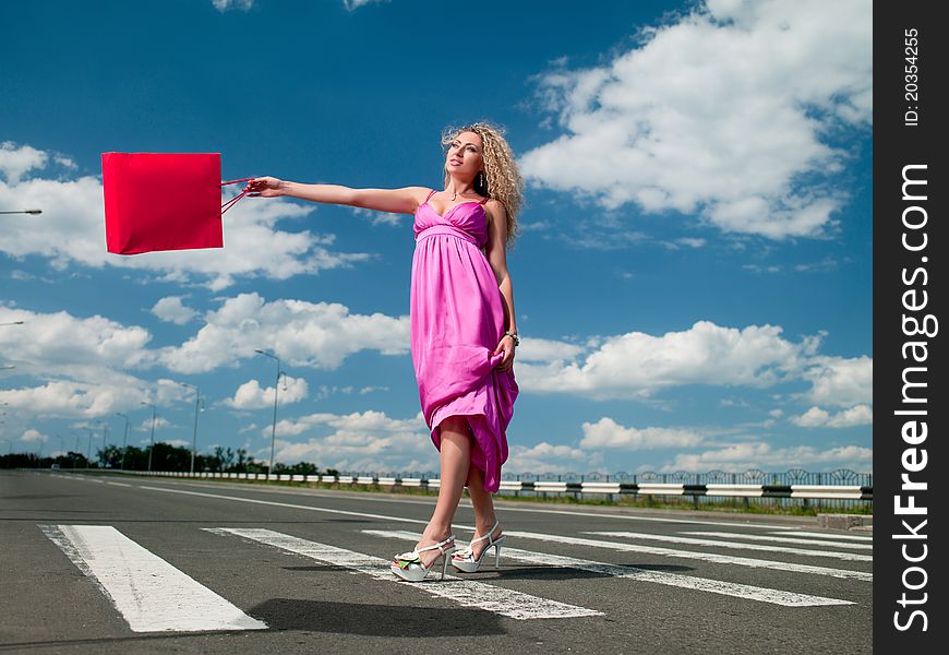 Woman in a pink dress with a bag goes over the road