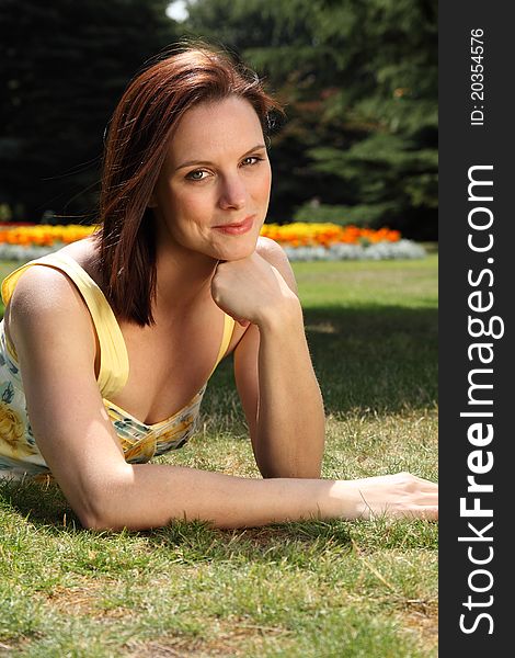 Portrait of happy smiling young woman lying on the grass in flower garden, wearing yellow summer dress and enjoying the beautiful summer sunshine. Portrait of happy smiling young woman lying on the grass in flower garden, wearing yellow summer dress and enjoying the beautiful summer sunshine.