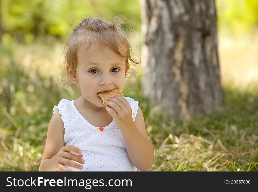 Little girl eating cracker in the park.