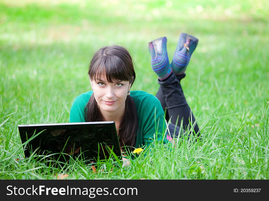 Beautiful young girl who lies with a laptop on a green lawn. Beautiful young girl who lies with a laptop on a green lawn