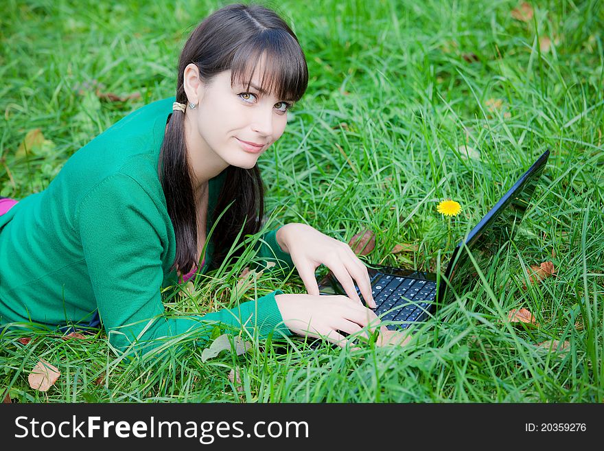 Beautiful young girl who lies with a laptop on a green lawn. Beautiful young girl who lies with a laptop on a green lawn