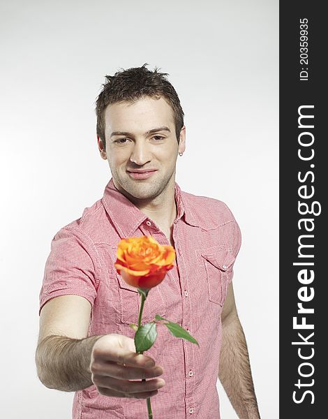 Handsome smiling young man extending his arm holding a rose. Handsome smiling young man extending his arm holding a rose