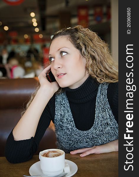 Beautiful girl with blond curly hair talking on a cell phone in cafe. Beautiful girl with blond curly hair talking on a cell phone in cafe