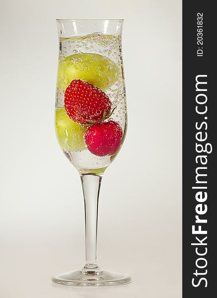 A champagne glass filled with sparkling water and various fruits. A champagne glass filled with sparkling water and various fruits