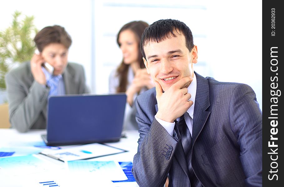 Smiling satisfied businessman looking at camera with his colleagues in the background during a meeting in the office