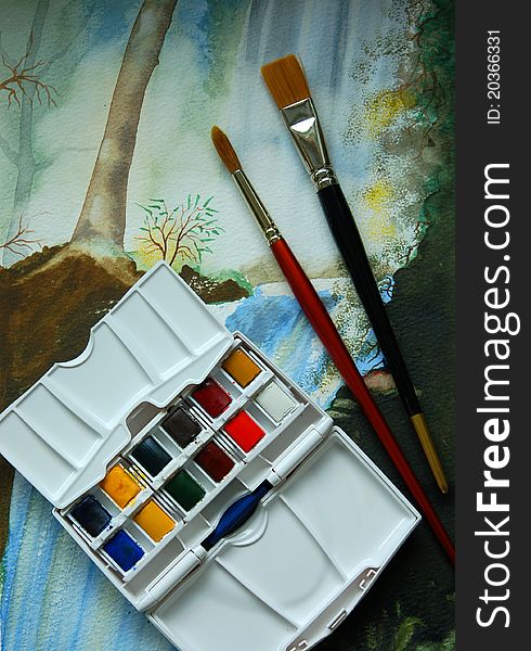 A box of watercolour paints and brushes displayed on a watercolour painting. A box of watercolour paints and brushes displayed on a watercolour painting