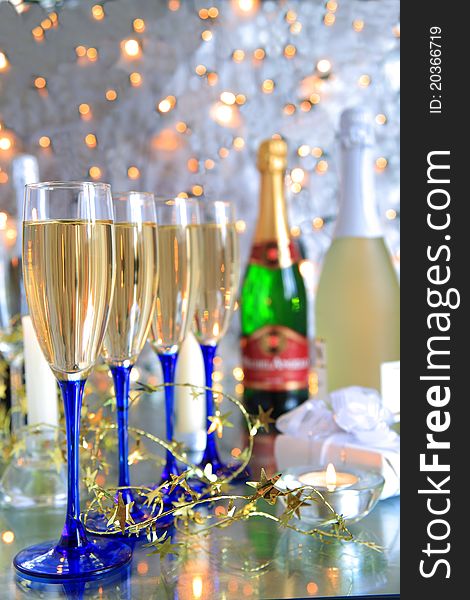 Champagne in glasses,bottles,candle,gift box on silver background with twinkle lights. Champagne in glasses,bottles,candle,gift box on silver background with twinkle lights.