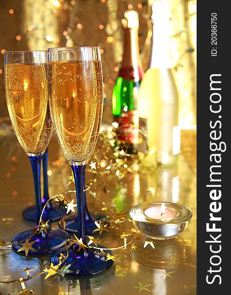 Close-up of champagne in glasses,candle light, bottles and twinkle lights on gold background.