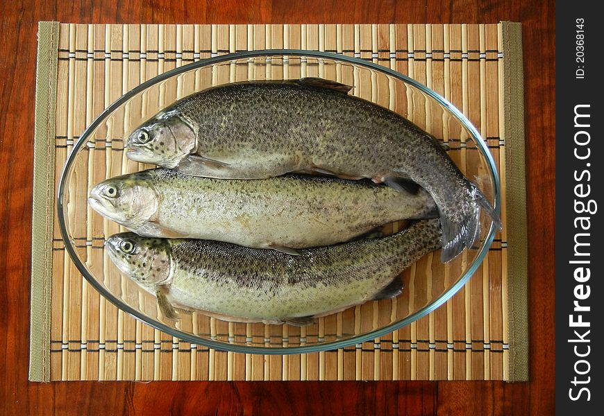 Three raw fishes in a glass bowl on a brown table. Three raw fishes in a glass bowl on a brown table