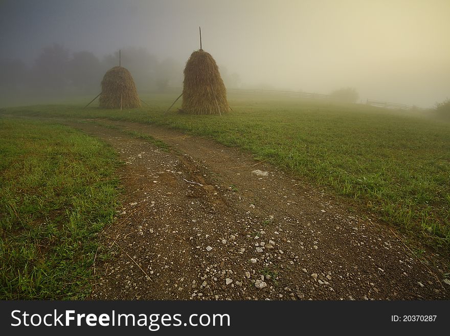 Road to the village with two haystacks on a misty morning.