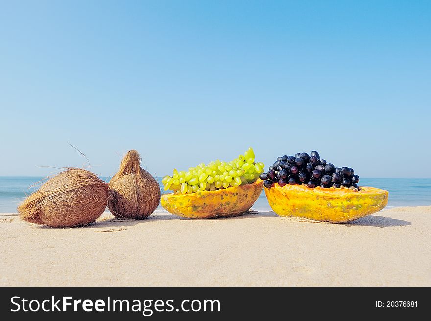 Papaya, coconut, nut and grapes on the sandy beach. Papaya, coconut, nut and grapes on the sandy beach