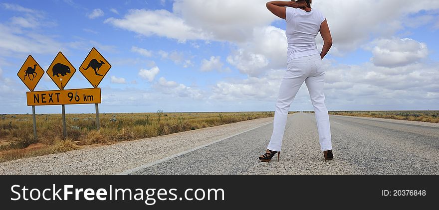 Attractive Woman standing beside famous Australian street sign in the middle of an endless highway, wearing high heel shoes. Attractive Woman standing beside famous Australian street sign in the middle of an endless highway, wearing high heel shoes.