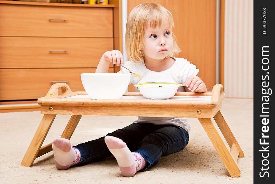 A small girl is sitting on the floor and is eating. A small girl is sitting on the floor and is eating